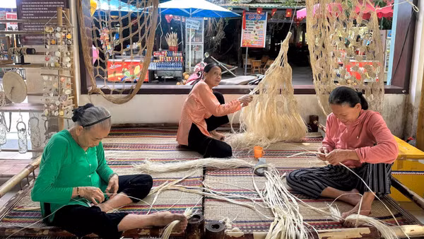 Nghệ nhân Lê Thị Kề (trái) hướng dẫn cách đan võng ngô đồng.