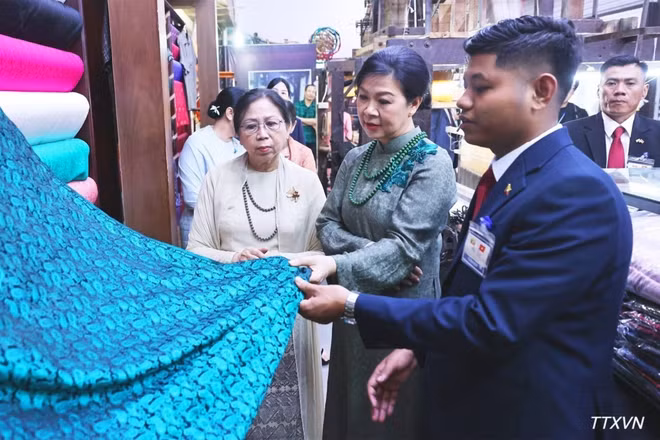 Phu nhân Ngô Phương Ly và Phu nhân Kyu Kyu Hla tham quan khu trưng bày sản phẩm lụa truyền thống và giới thiệu các sản phẩm đặc sắc của làng nghề Vạn Phúc. (Ảnh: TTXVN)